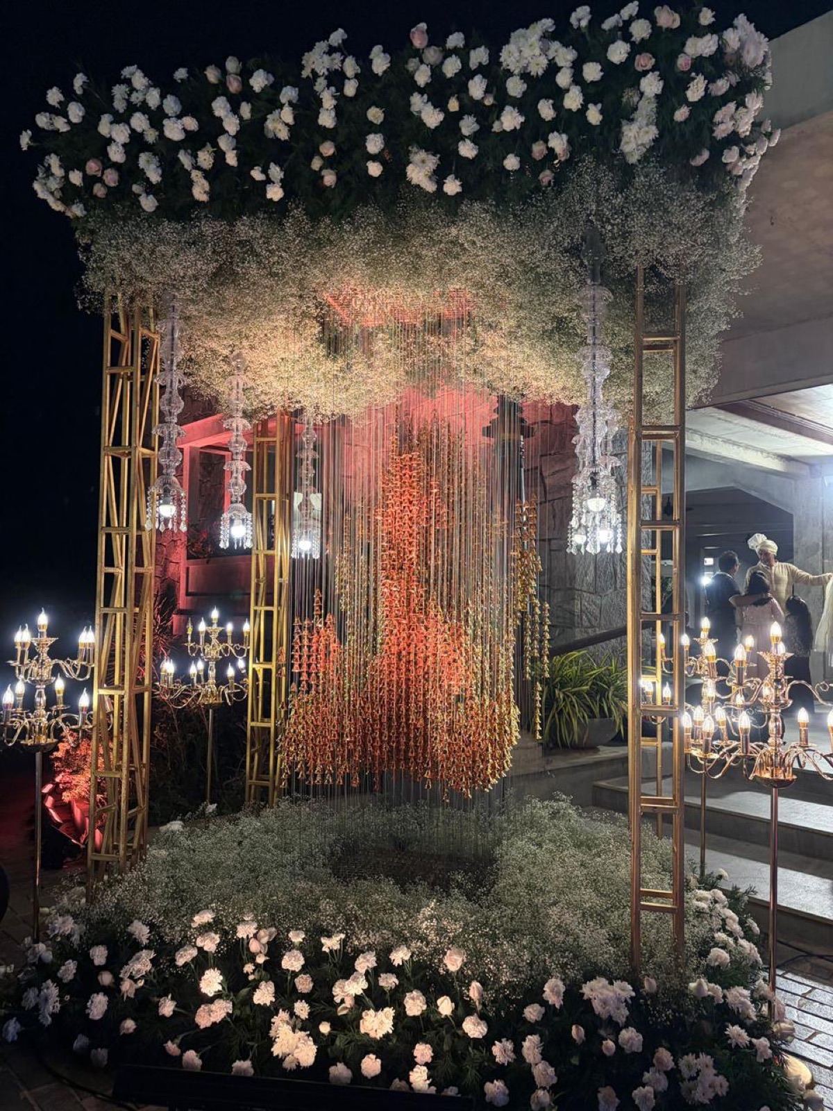 Night mandap of white roses and baby's breath with a curtain of hanging golden bells and crystal candelabras — Panigrahana decor
