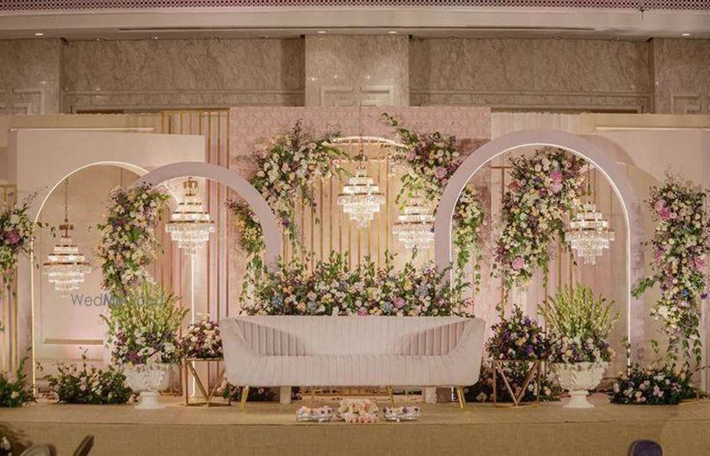 Blush arched reception backdrop with crystal chandeliers, pink and ivory flowers and a pale curved sofa