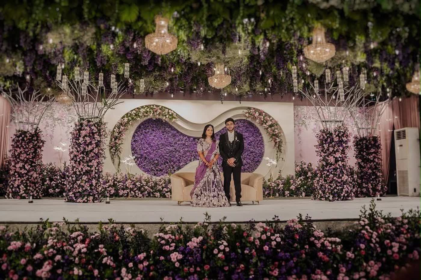 Lavender and orchid reception stage with a heart-form floral centre, floral columns and a suspended wisteria ceiling