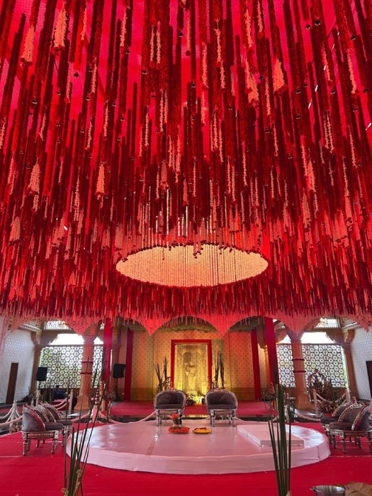 Thousands of hanging crimson and ivory floral strings forming a dramatic ceiling above a round white stage — Panigrahana decor