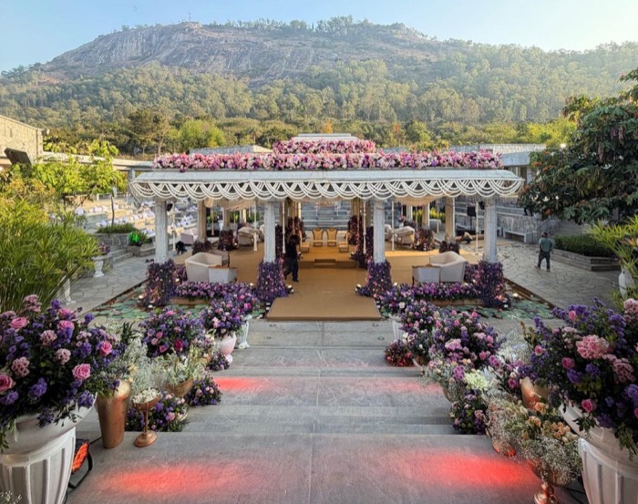 Open hillside pavilion crowned with pink and lavender florals and pearl swags, mountain backdrop — Panigrahana decor