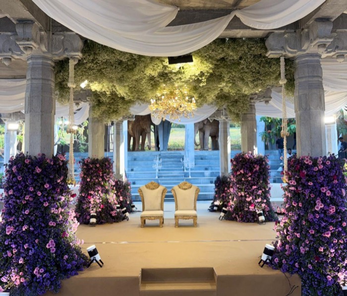 Stone-pillared pavilion dressed in purple and pink floral columns under a baby's breath ceiling and chandelier — Panigrahana decor