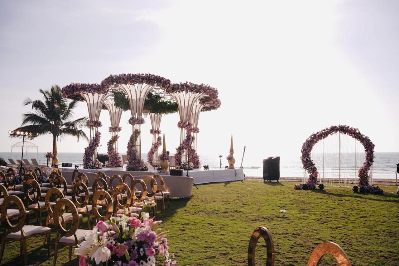 Floral mandap and arches on a seafront lawn beside palm trees