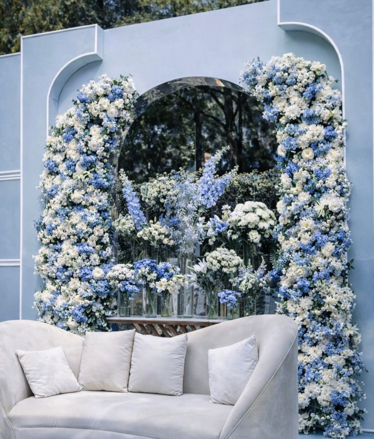 Blue hydrangea and white rose arch framing a white lounge sofa