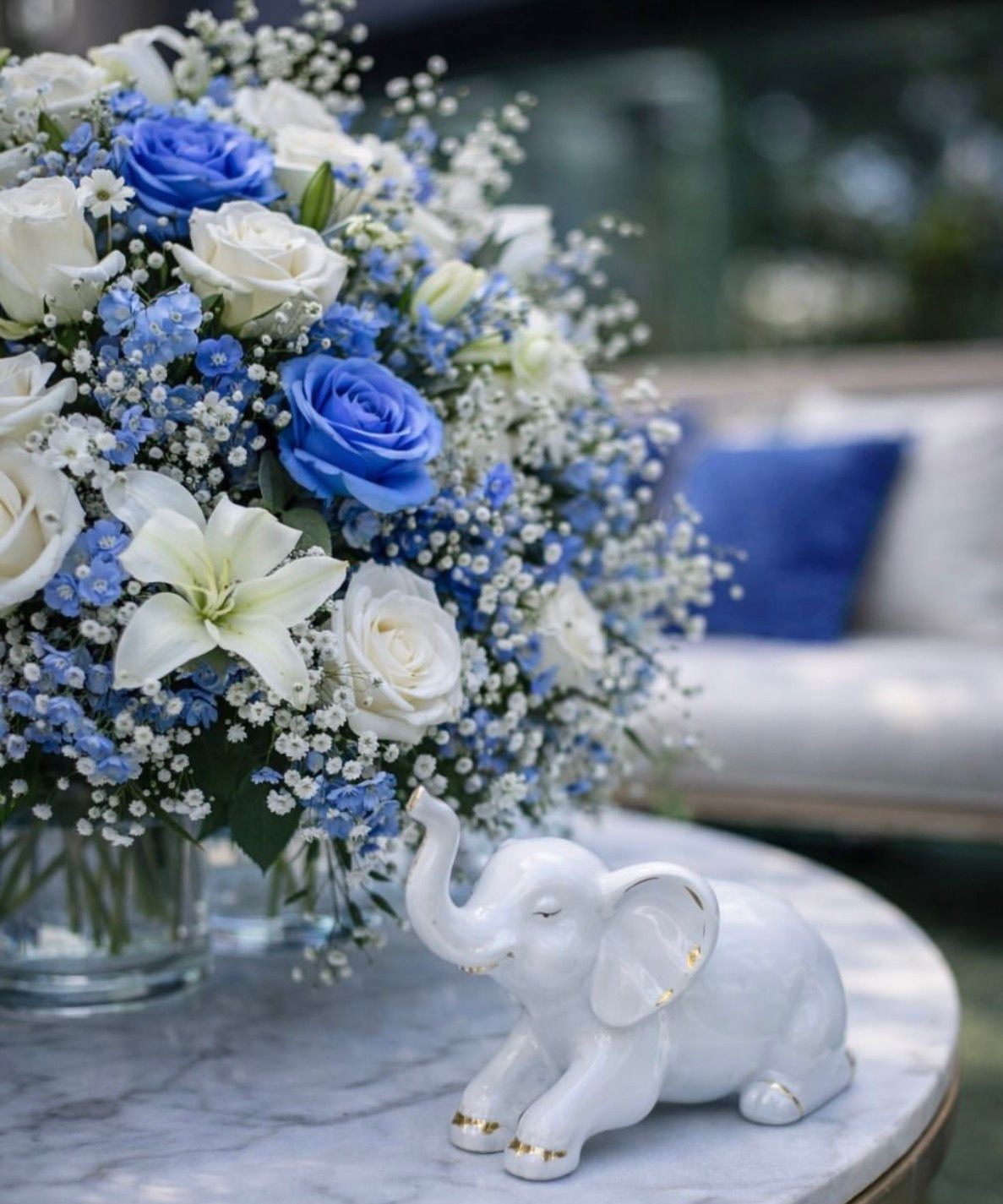 Blue rose arrangement beside a white elephant figurine on a marble table