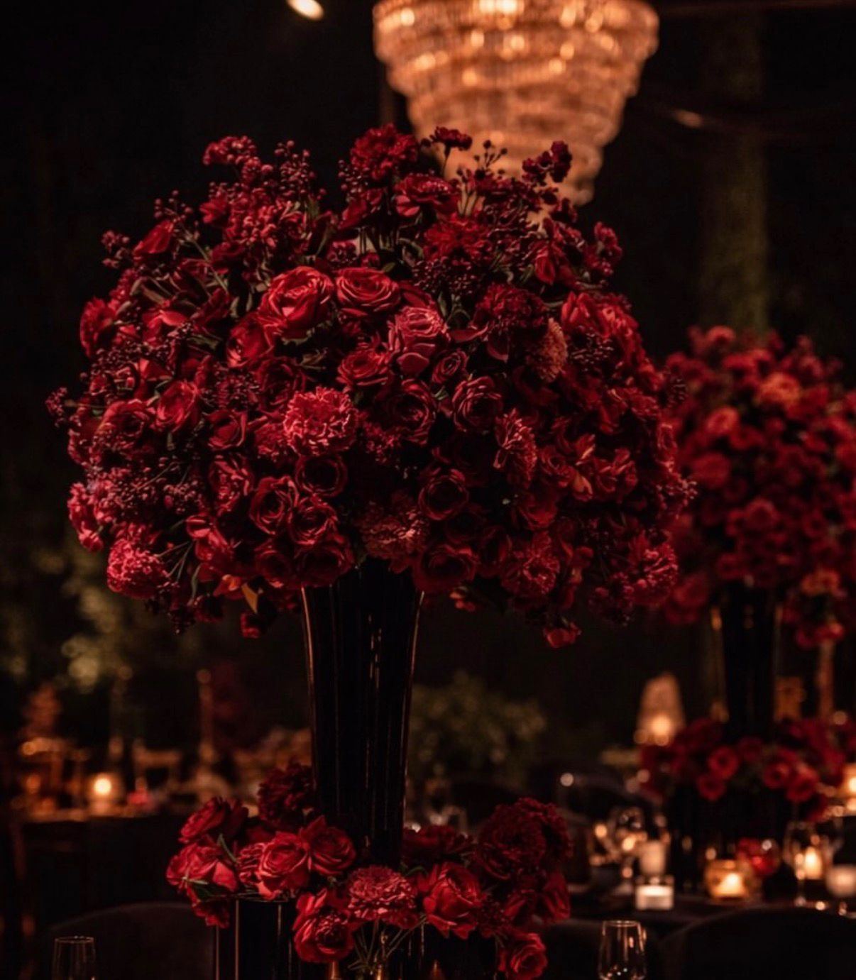 Tower of burgundy roses ringed by candles at an evening reception