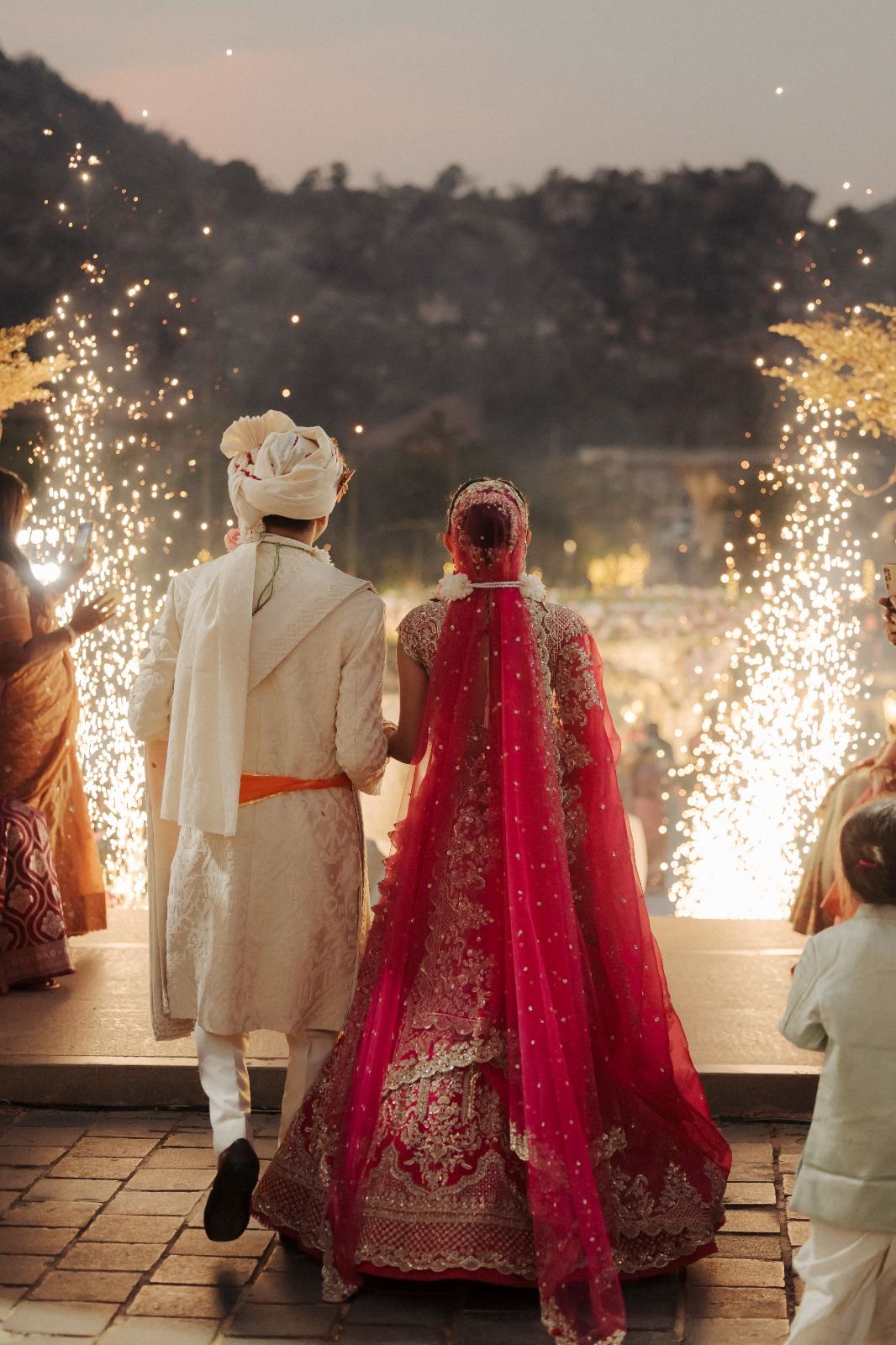 Bride and groom entering through cold pyrotechnics in evening light