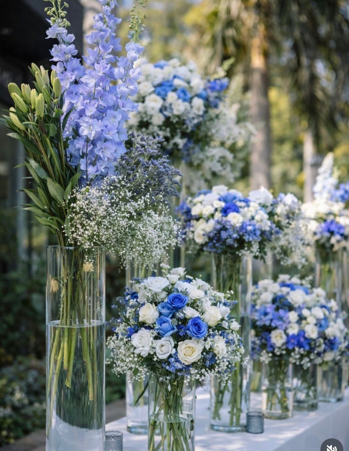 Glass vases of blue delphinium, hydrangea and white roses on a table