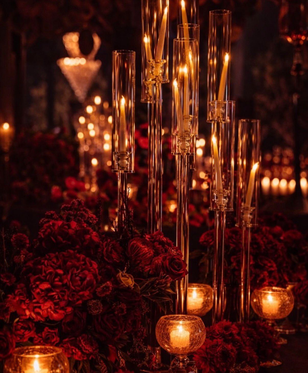 Tall glass candle stems rising from a bed of red roses
