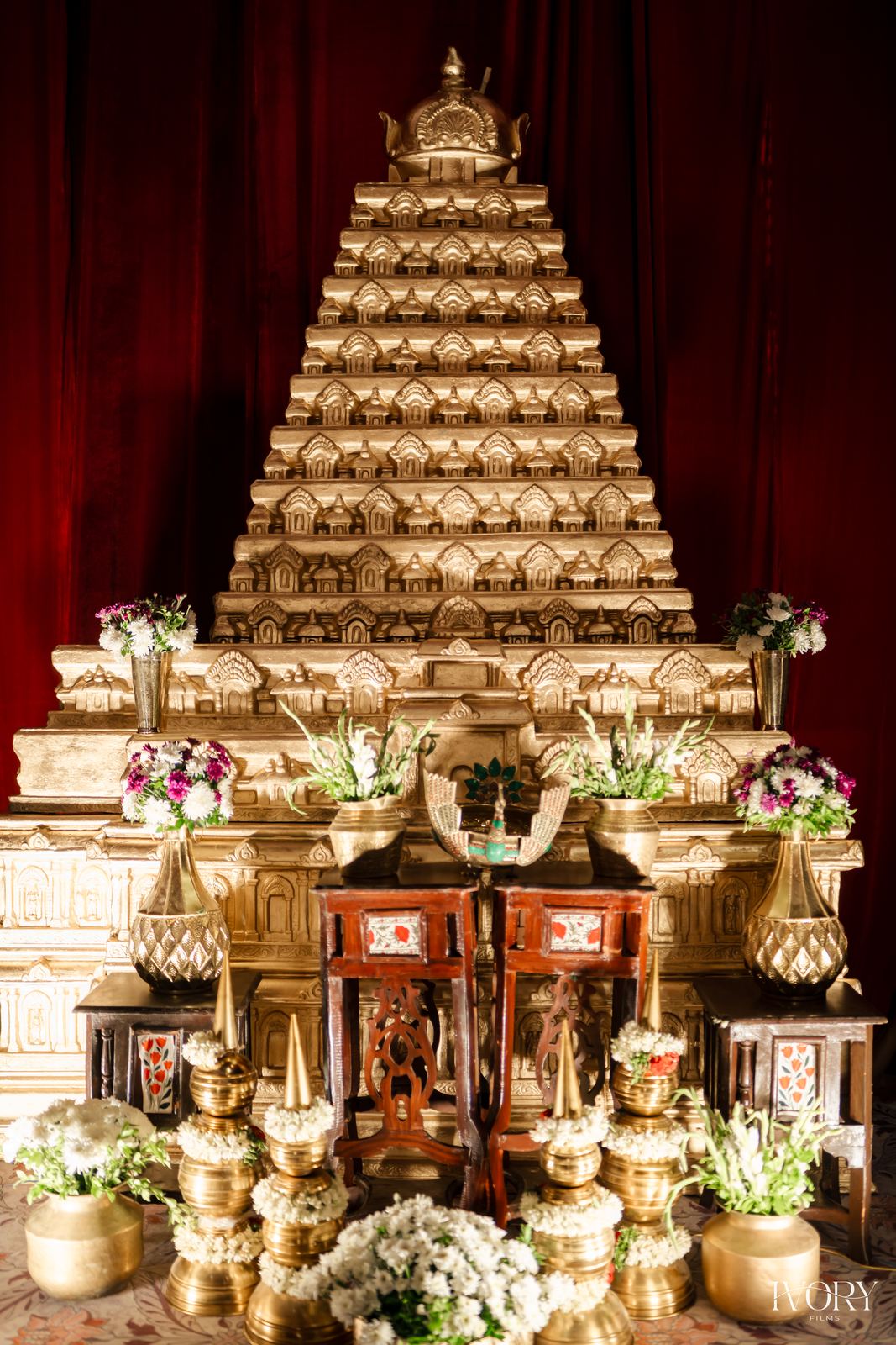 Gold tiered temple tower backdrop with white garlands and brass urns