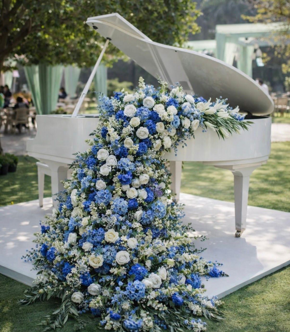 White grand piano with a cascade of blue and white flowers on a lawn