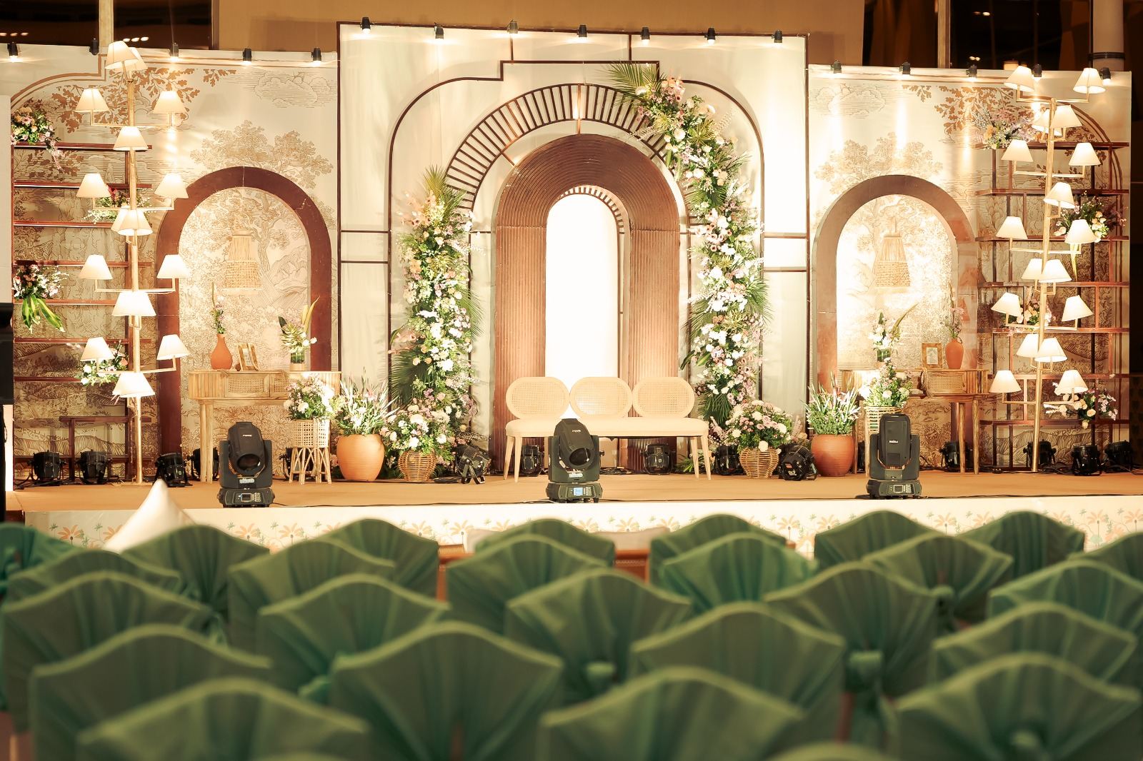 Pastel arched stage backdrop with lamps and pleated green guest seating