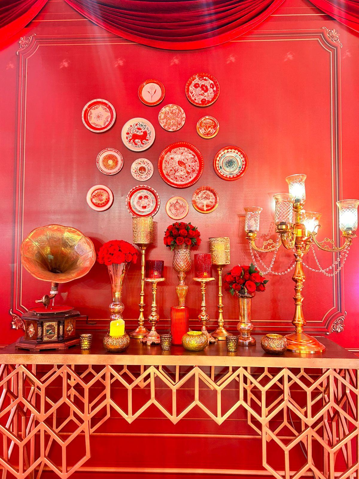 Deep red backdrop styled with vintage plates, gramophone and brass candelabra