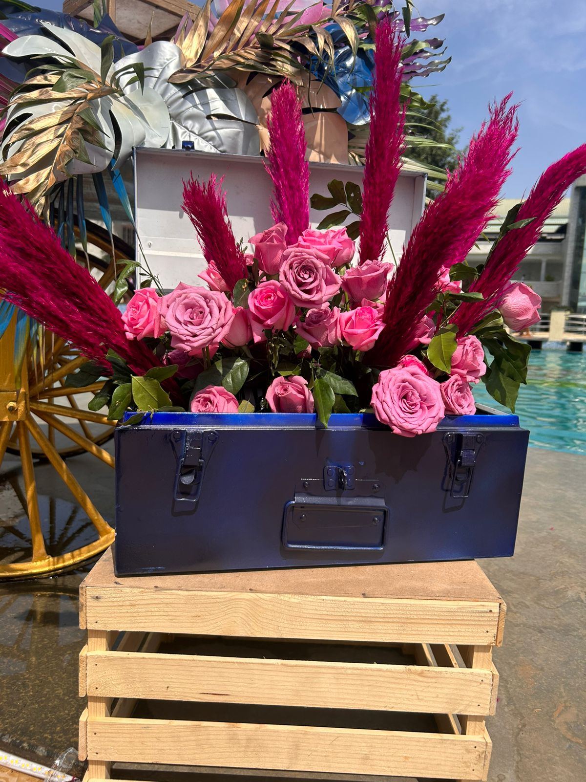 Pink roses and pampas in a blue trunk on wooden crates poolside