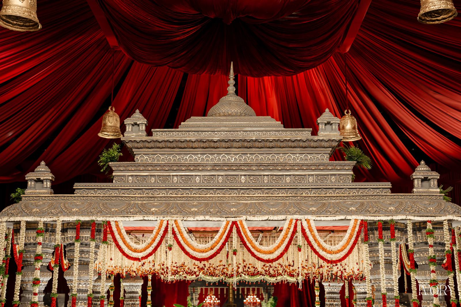 Silver carved mandap structure under deep red drapes with marigold garlands, a Panigrahana build