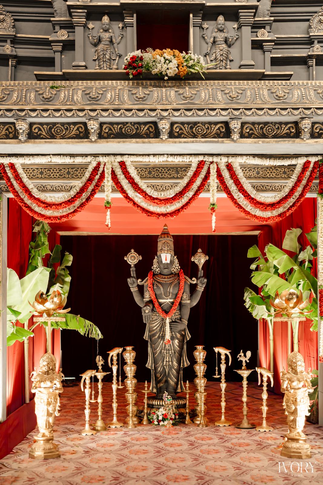 Stone-finish temple facade mandap with deity idol, red canopy and brass lamps