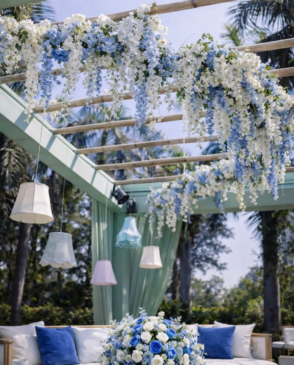 White wisteria strands on a pale pergola with hanging pleated lamps