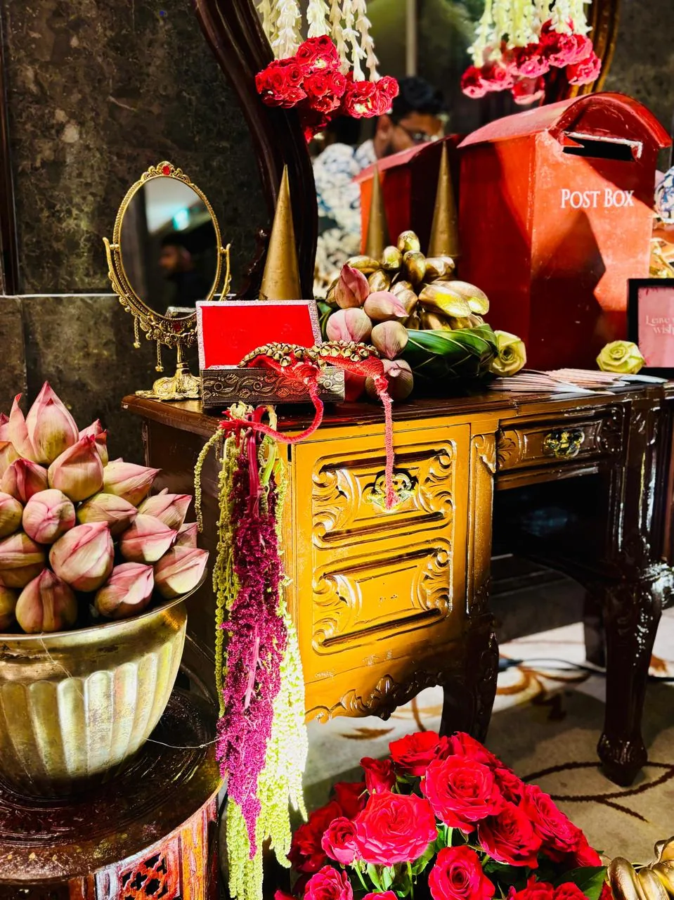 Carved wooden desk with a gold vanity mirror, a velvet box of ghungroo anklet bells, pink lotus buds, gold-dipped buds, hanging amaranthus and a red post box