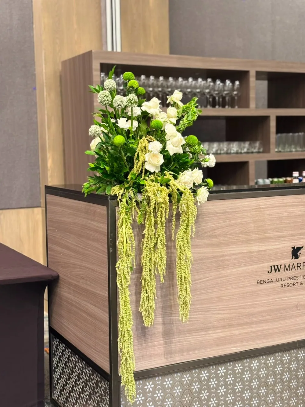 White roses, green button chrysanthemums and allium over a fall of green amaranthus on the bar counter at JW Marriott Bengaluru Prestige Golfshire. Panigrahana Weddings.