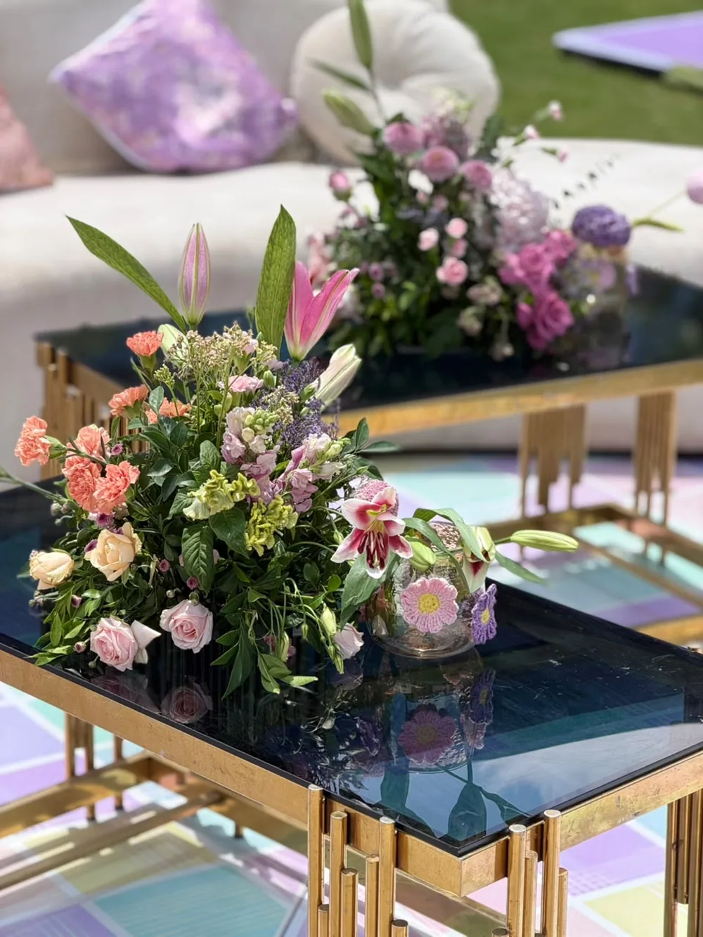 Low pastel arrangements of lilies, lisianthus, spray roses and coral carnations on gold and smoked-glass tables over a pastel checkerboard floor at JW Marriott Bengaluru Prestige Golfshire. Panigrahana Weddings.