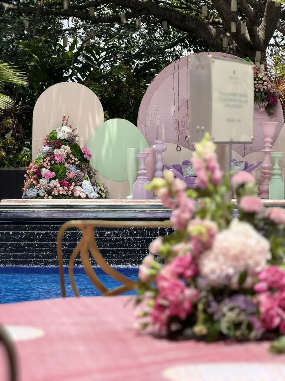 Blush and mint arched backdrops with pastel urns and a floral mound set along the pool edge at JW Marriott Bengaluru Prestige Golfshire. Panigrahana Weddings.