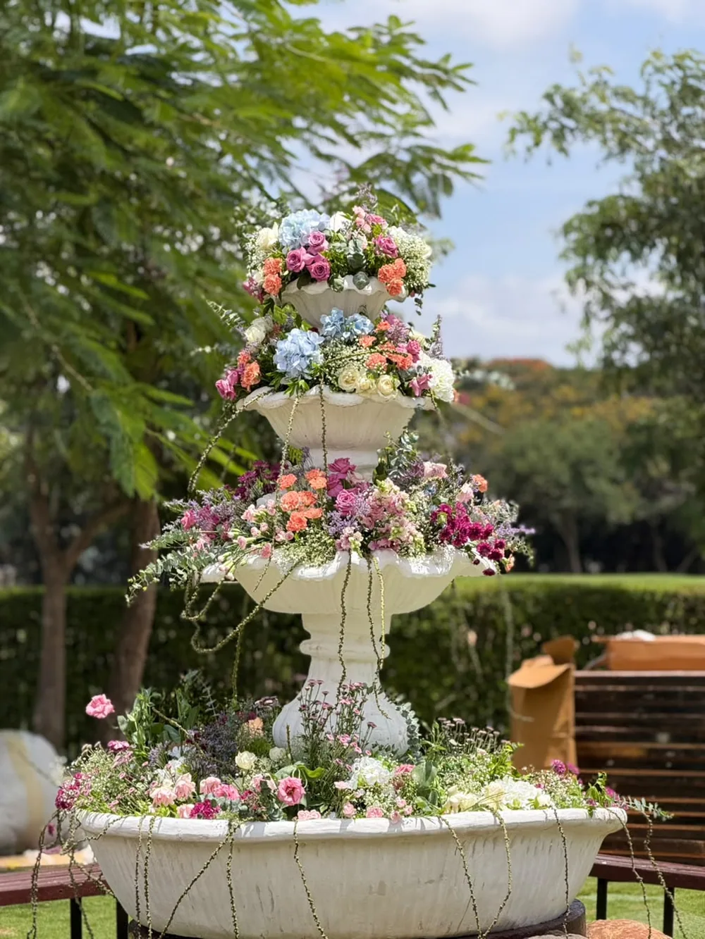 A three-tier stone fountain planted with blue hydrangea, spray roses, carnations and trailing amaranthus on the lawn at JW Marriott Bengaluru Prestige Golfshire. Panigrahana Weddings.