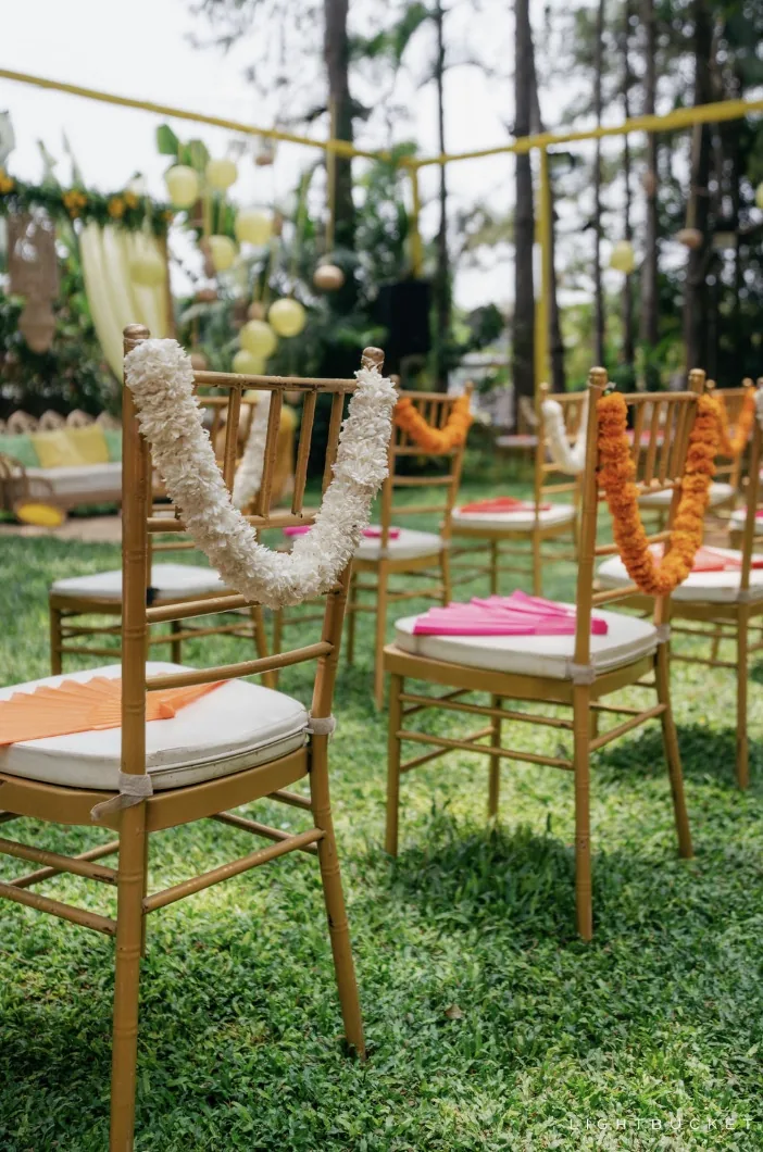 Gold Chiavari chairs draped in white jasmine and orange marigold garlands for the haldi on the lawn at Nature Knots, Bangalore