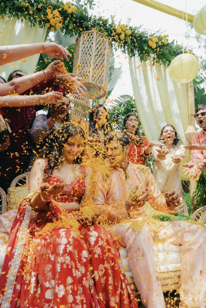 Family showering marigold petals on the couple during the haldi under the lemon lanterns at Nature Knots, Bangalore
