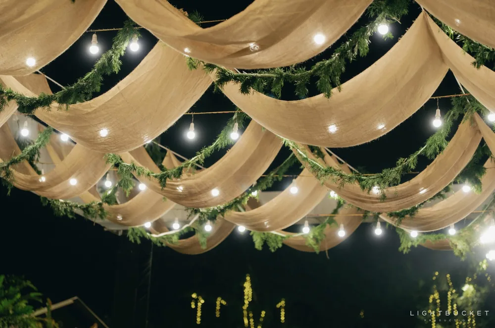 Jute fabric canopy swags with fern garlands and filament bulbs over the sangeet lawn at night at Nature Knots, Bangalore