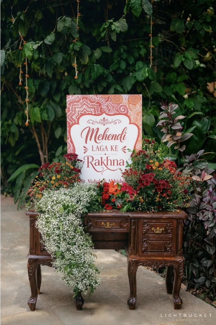 Mehendi sign on a carved vintage desk spilling baby's breath and red roses against greenery at Nature Knots, Bangalore