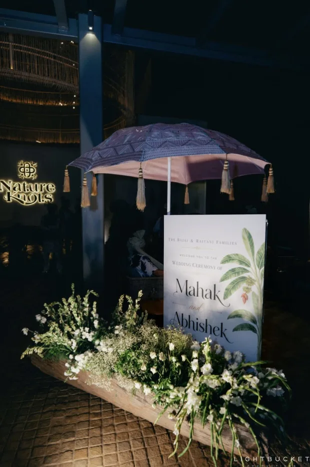 Night welcome display at the Nature Knots entrance, Bangalore: a sign with a banana-leaf motif, a fringed parasol and white florals in a long planter