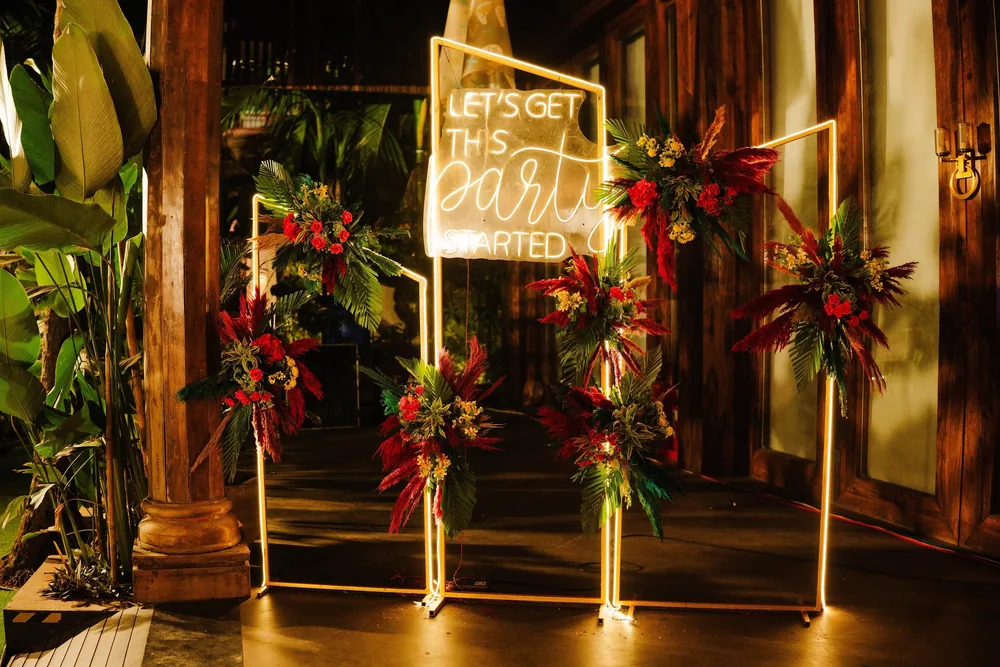 After-party neon sign at Riva Beach Resort, Goa: 'Let's get this party started' on lit frames, dressed with red roses, red pampas plumes and palm leaves.