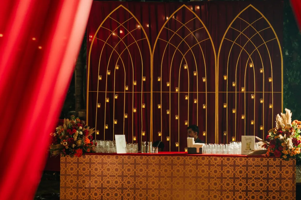Mehendi bar at Riva Beach Resort, Goa: three gold arch frames hung with candle votives against maroon velvet, a geometric-print counter and flowers with pampas.