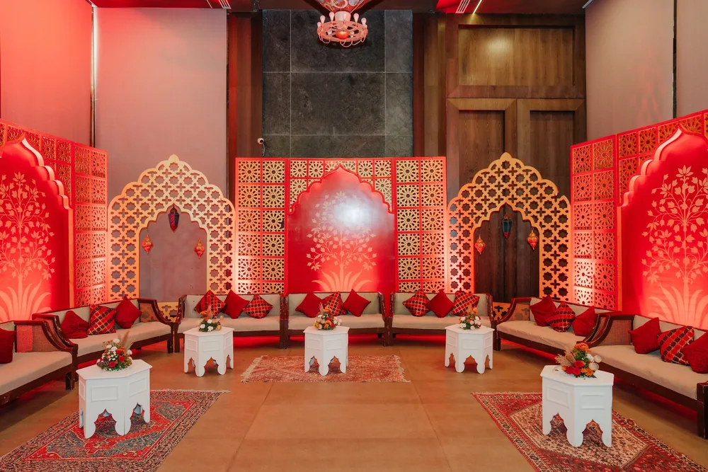 Mehendi majlis lounge at Riva Beach Resort, Goa: red and gold jaali arch screens, low cream sofas with red cushions, white hexagonal side tables and rugs.