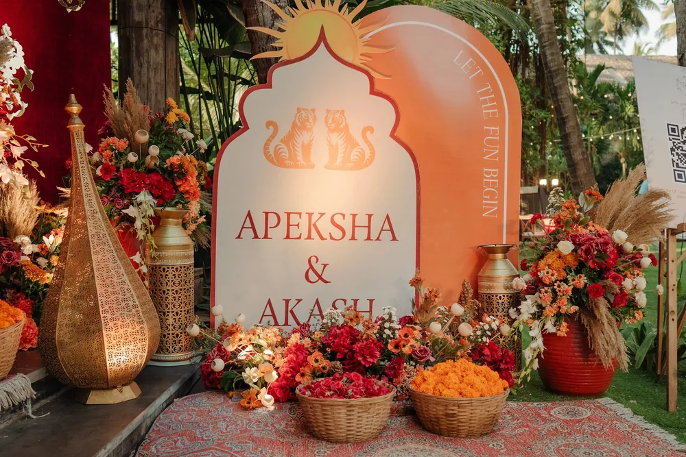 Mehendi welcome sign at Riva Beach Resort, Goa, with twin tigers and a sun motif, a brass jaali lantern, pampas grass, red flowers and baskets of marigolds.