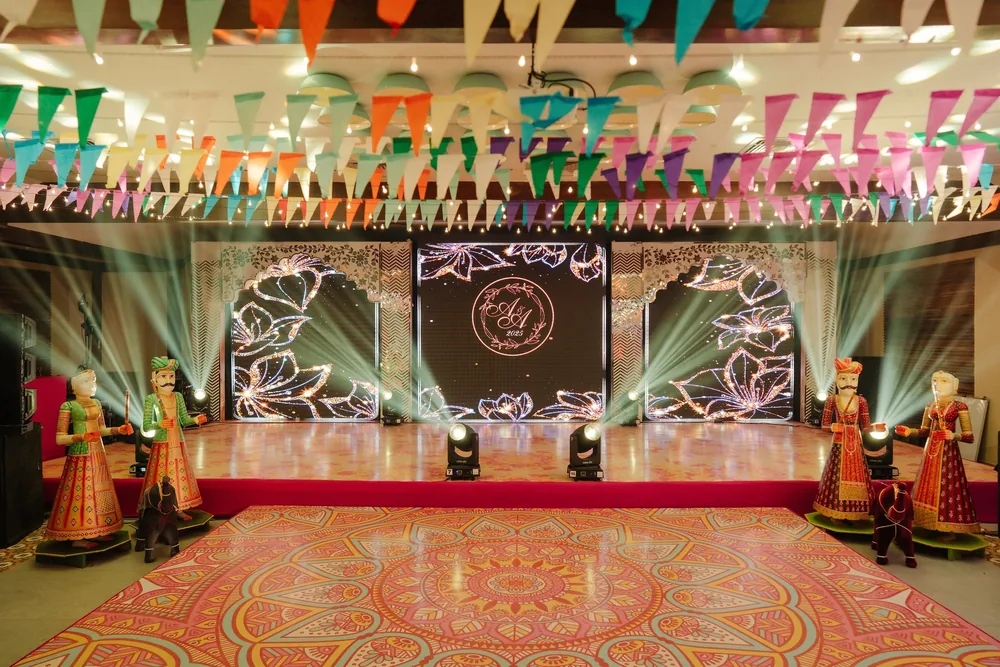 Sangeet stage at Riva Beach Resort, Goa: LED screens with lotus art and an A&A monogram, white jaali arches, painted puppets, bunting and a mandala dance floor.