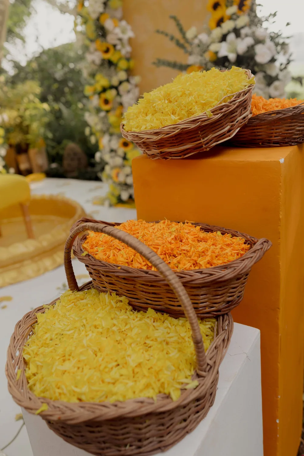 Wicker baskets heaped with yellow and orange marigold petals on white and orange plinths beside the haldi stage at Beleza by the Beach, Goa.