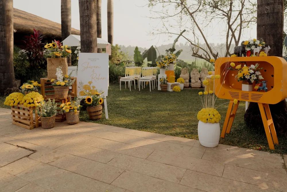 Haldi welcome path at Beleza by the Beach, Goa: wooden crates and wicker baskets of sunflowers, a welcome board and an orange retro TV-shaped flower stand.