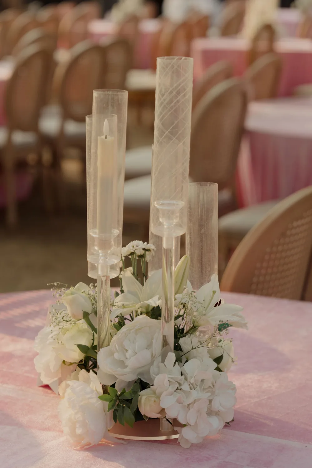 Reception centrepiece at Beleza by the Beach, Goa: clear glass cylinders over taper candles above white lilies, roses and hydrangea on a pink tablecloth.