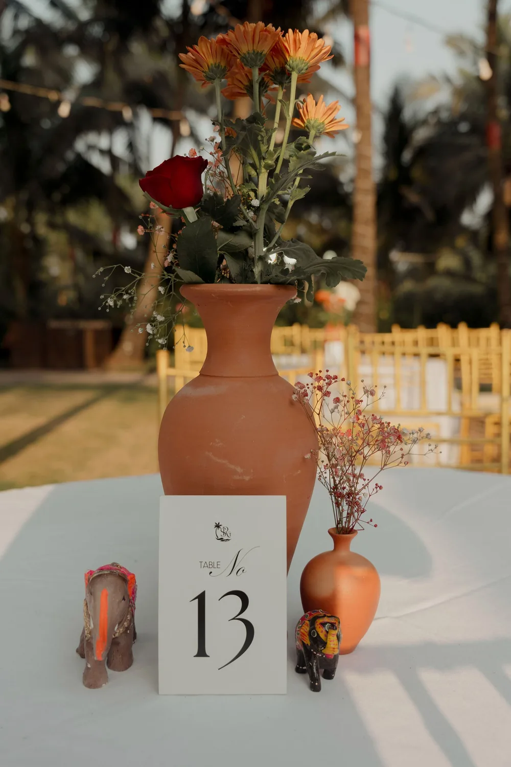 Sangeet table detail at Beleza by the Beach, Goa: terracotta vases of orange gerberas and a red rose, painted elephant figurines and a monogrammed table card.