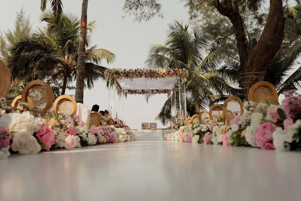 Wedding mandap at Beleza by the Beach, Goa: clear acrylic posts and a floral canopy at the end of a white aisle edged with pink and white flowers.