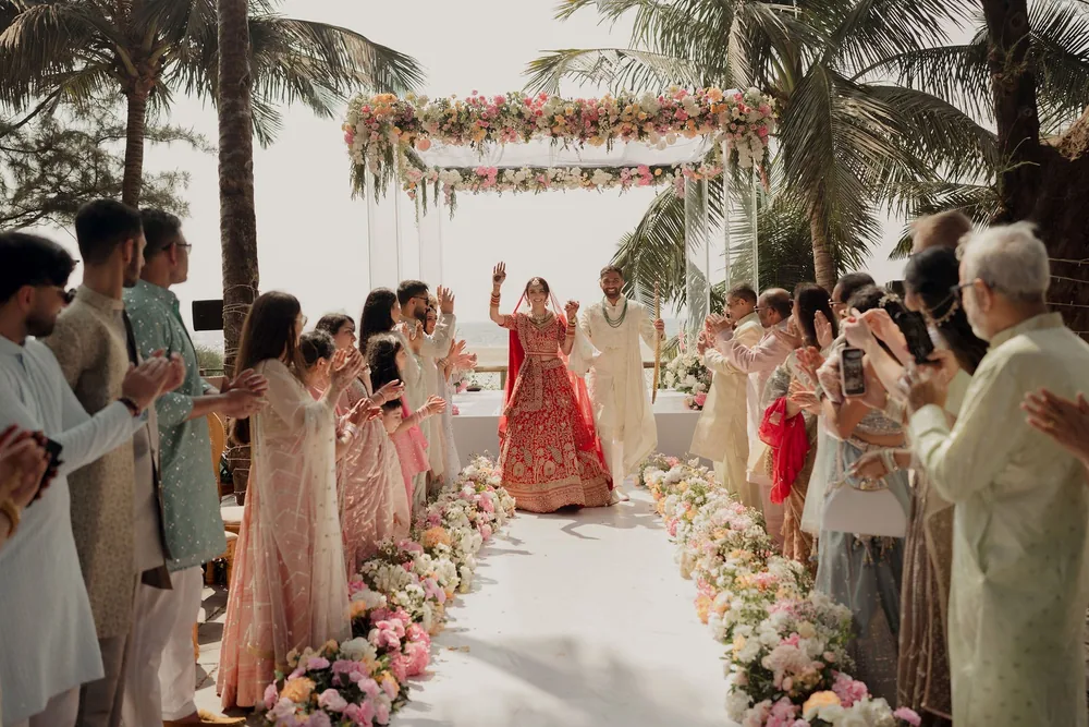 Guests applaud as Shivani and Rohan walk away from the flower-canopied mandap down the white wedding aisle lined with flowers at Beleza by the Beach, Goa.