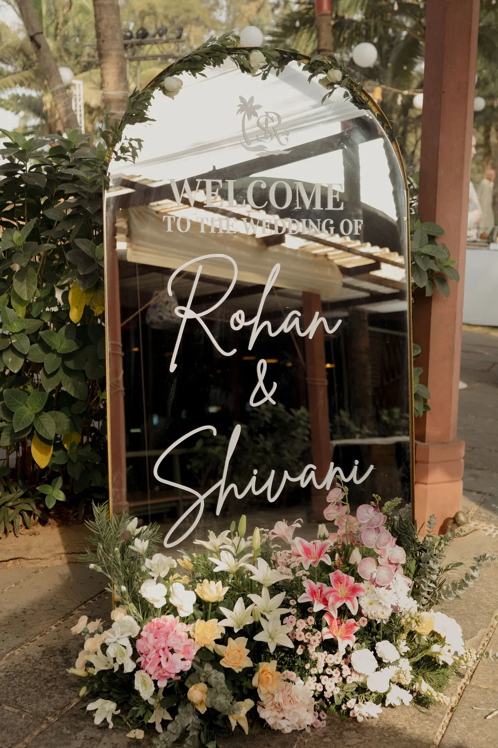 Arched mirror sign welcoming guests to the wedding of Rohan & Shivani at Beleza by the Beach, Goa, set in a bed of lilies, pink orchids, roses and hydrangeas.