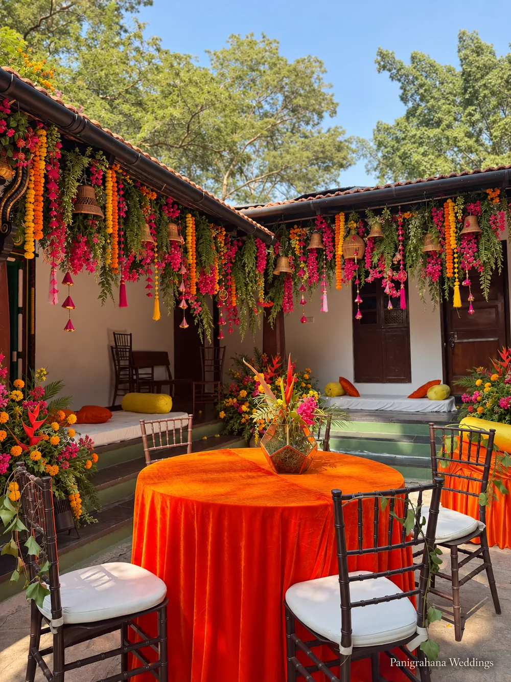 Courtyard of The Tamarind Tree set for a haldi lunch, with orange velvet tables and verandahs hung with floral canopies of marigold, bougainvillea and foliage