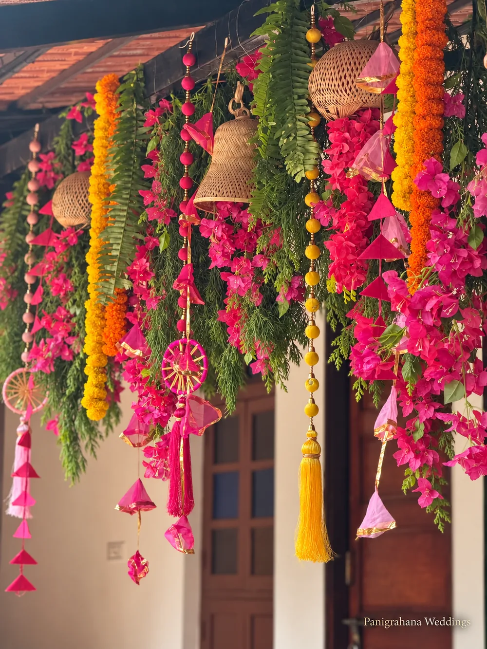 Verandah canopy hung with marigold strings, pink bougainvillea, ferns, cane bells, pink paper cones, thread wheels and yellow tassels for a haldi
