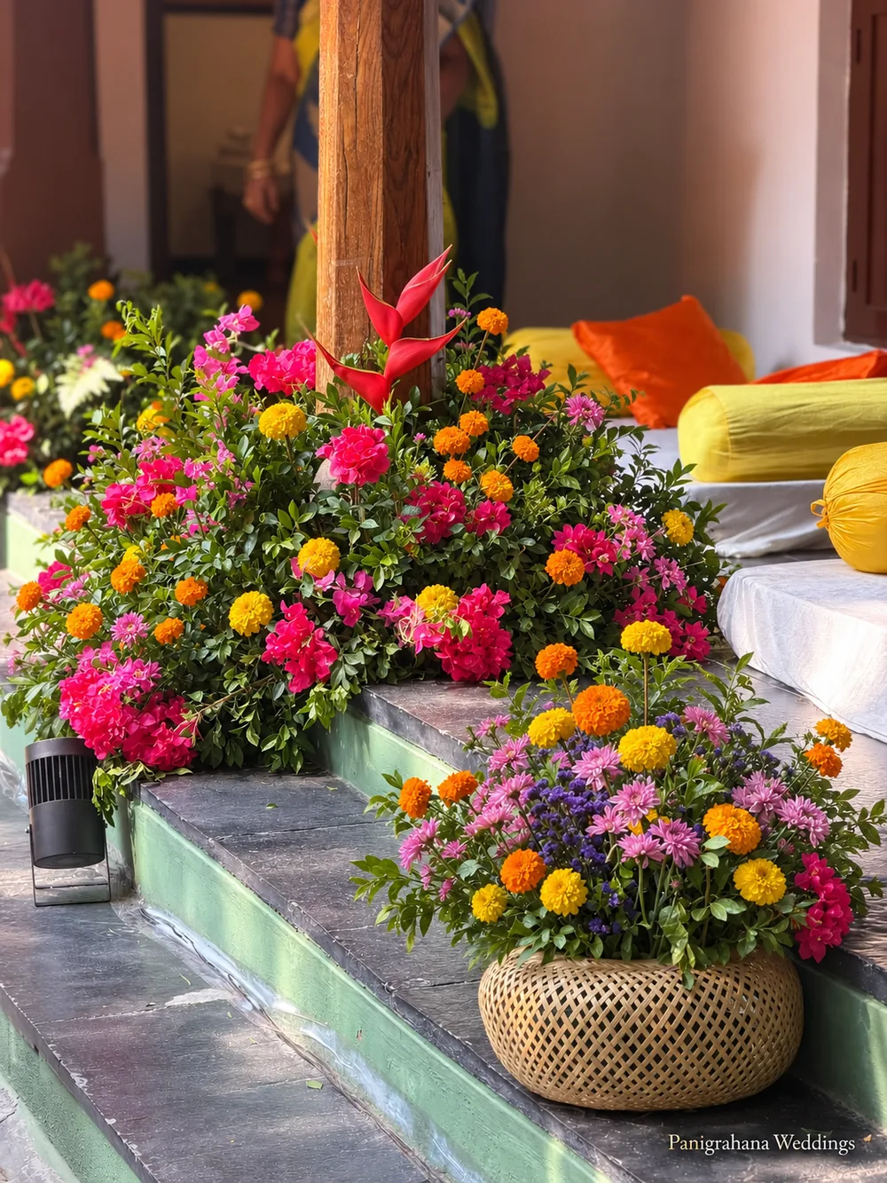 Verandah steps dressed with bowls of marigold, pink and orange mixed flowers and a cane basket arrangement beside orange and yellow cushions