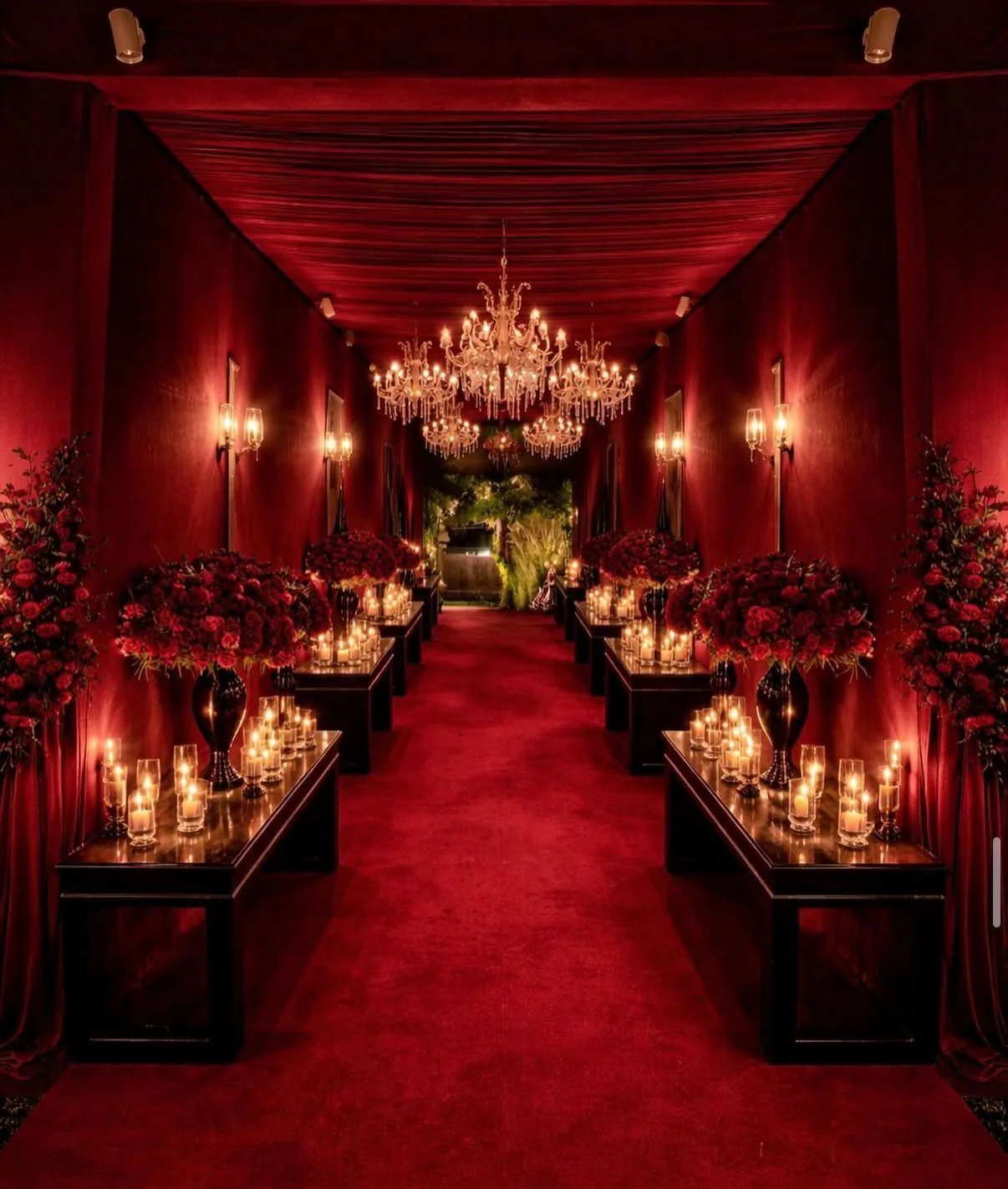 A red velvet corridor lit by chandeliers and candles