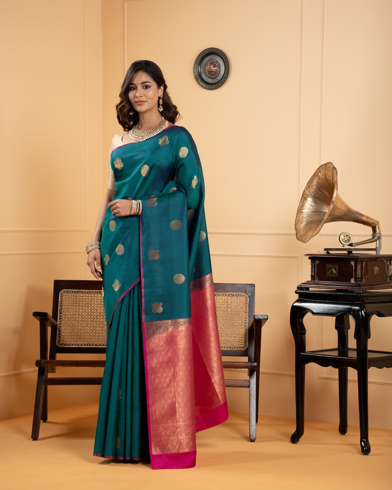 Teal Kanchivaram silk saree with gold buttas and a pink and gold pallu, worn by a model