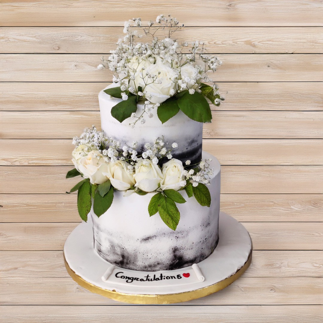Two-tier white cake in a naked buttercream finish with fresh white roses, baby's breath and leaves