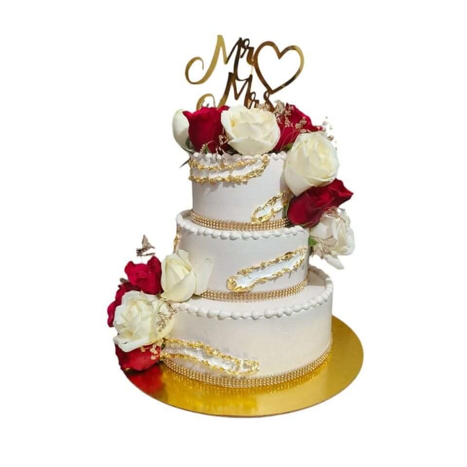 Three-tier white wedding cake with gold detailing, red and white roses and a Mr & Mrs topper